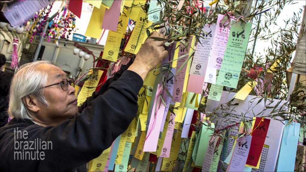 Japanese Brazilian man holds a colorful strip of paper bearing personalized wishes during Liberdade's Tanabata Matsuri festival.