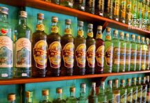 Brazilian Cachaça Explained: Dozens of cachaça bottles from various distillers line the wooden shelves, side by side.