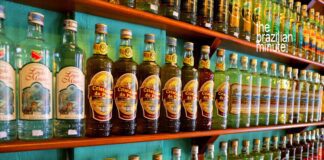 Brazilian Cachaça Explained: Dozens of cachaça bottles from various distillers line the wooden shelves, side by side.