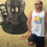 Brazilian guitarist Phill Fest Sings a Slice of Life, standing in front of a yelllow wall featurng a street art guitar.