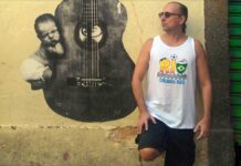 Brazilian guitarist Phill Fest Sings a Slice of Life, standing in front of a yelllow wall featurng a street art guitar.
