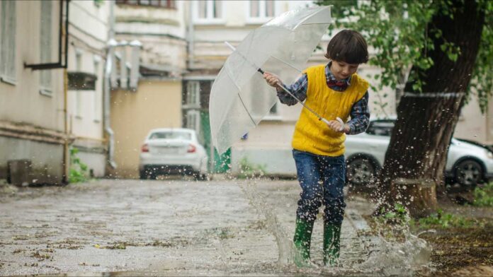 Boy-In-Rain-02 The Waters of March 50th Anniversary. A Young boy plays in a rain puddle while holing a small umbrella.